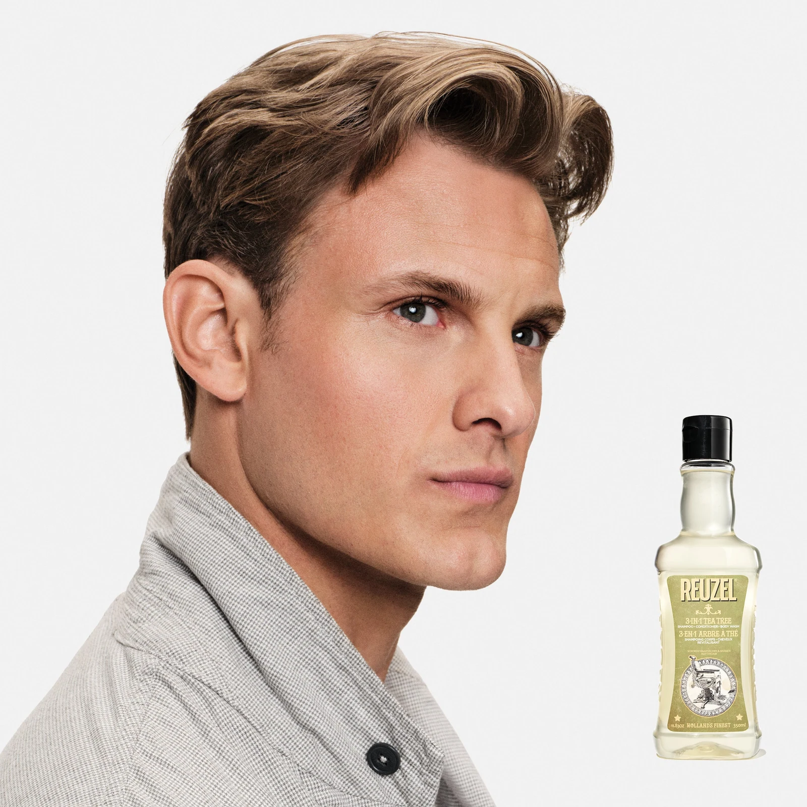 Model with short hair with a bottle of Reuzel 3-in-1 Tea Tree Shampoo on a white background