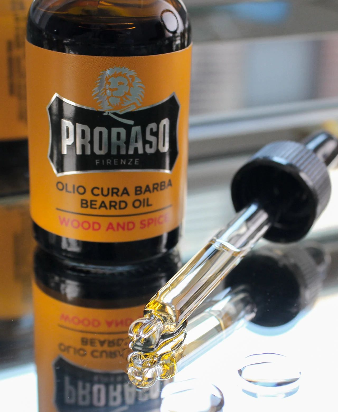 Proraso - Beard Oil - Wood & Spice - 100ml: Wood & Spice Beard Oil bottle with dropper sitting on top of mirror with visible drops and oil in vial, view 2