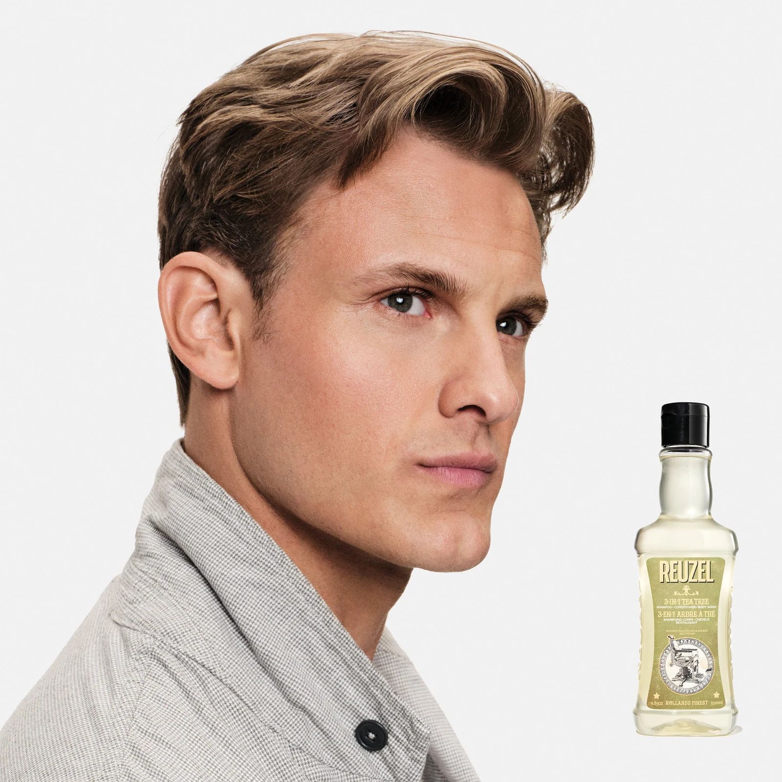 Model with short hair with a bottle of Reuzel 3-in-1 Tea Tree Shampoo on a white background