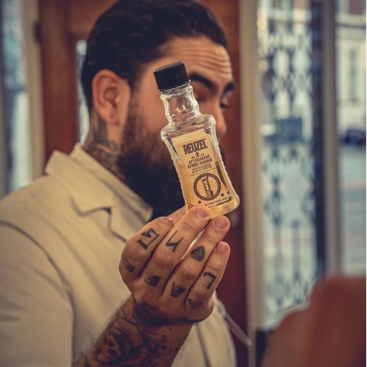 Barber holding a bottle of Reuzel Wood & Spice Aftershave 100ml in a barbershop