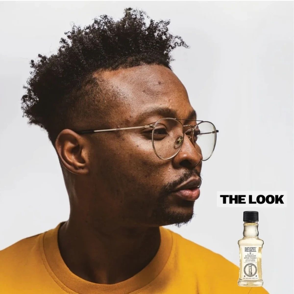 Man with a trimmed goatee and curly high top beside Reuzel Wood & Spice Aftershave 100ml